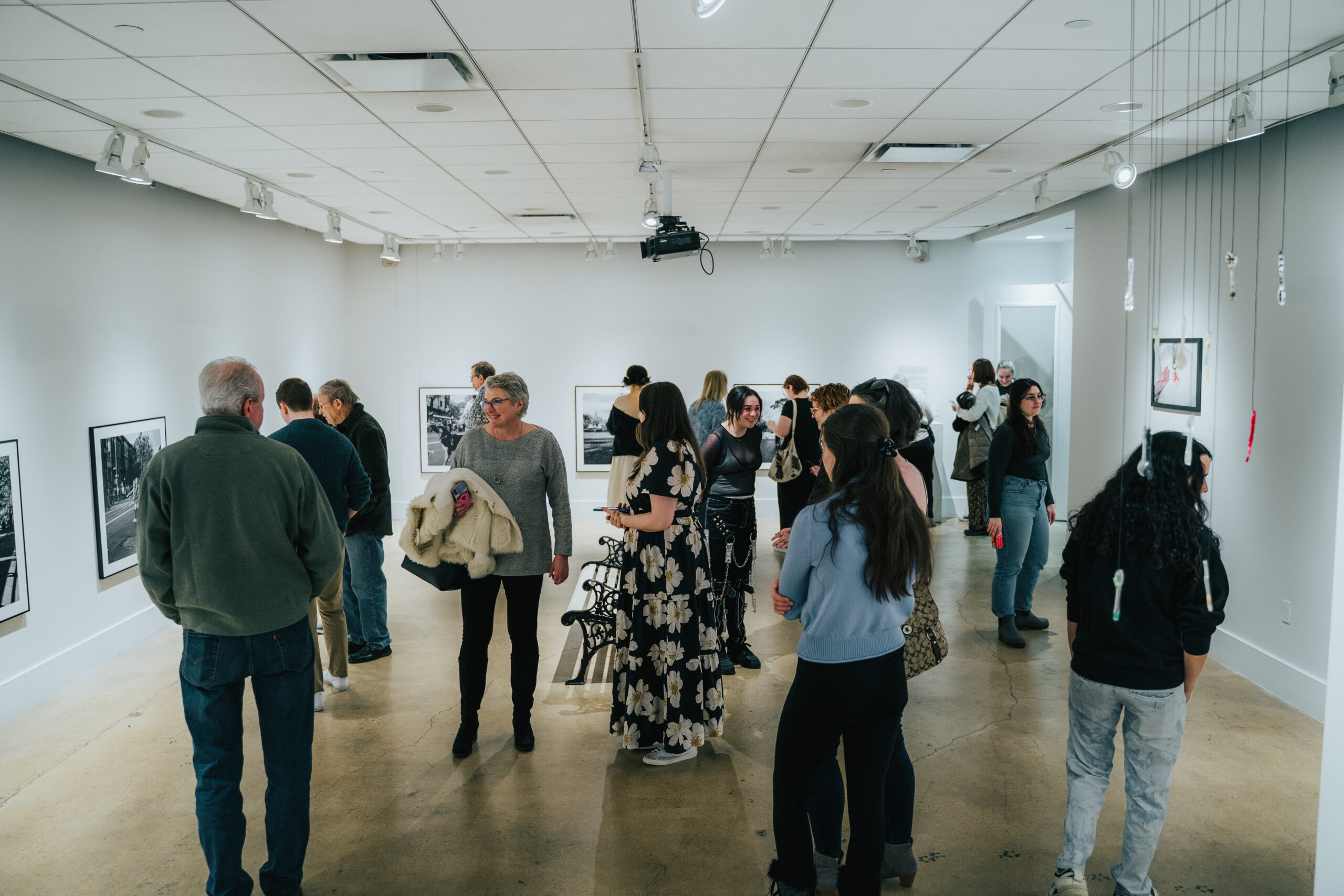 A gallery with photographs on the wall, full of people looking at the artwork.