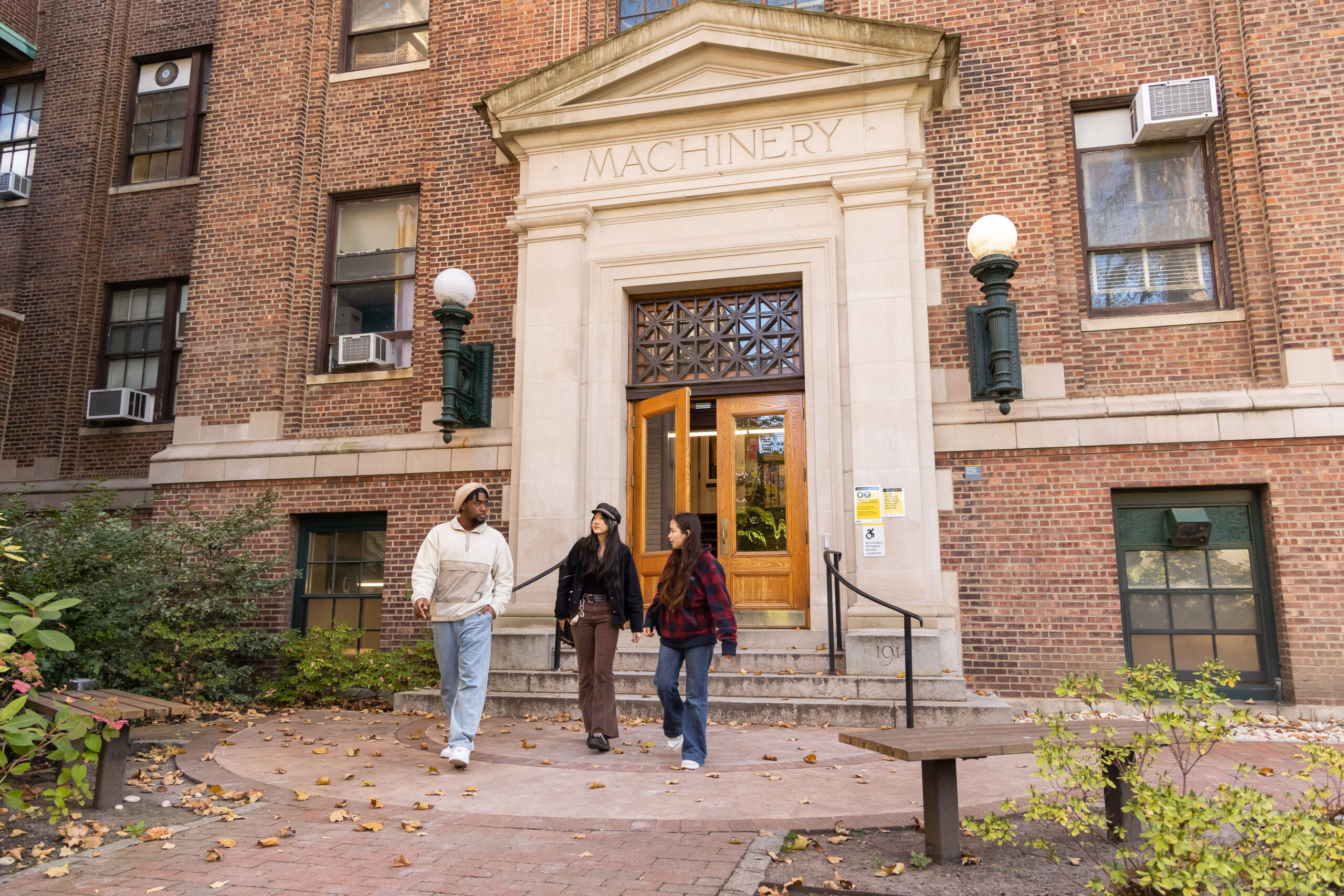 A photograph of three students walking outside a historic brick building with the word 