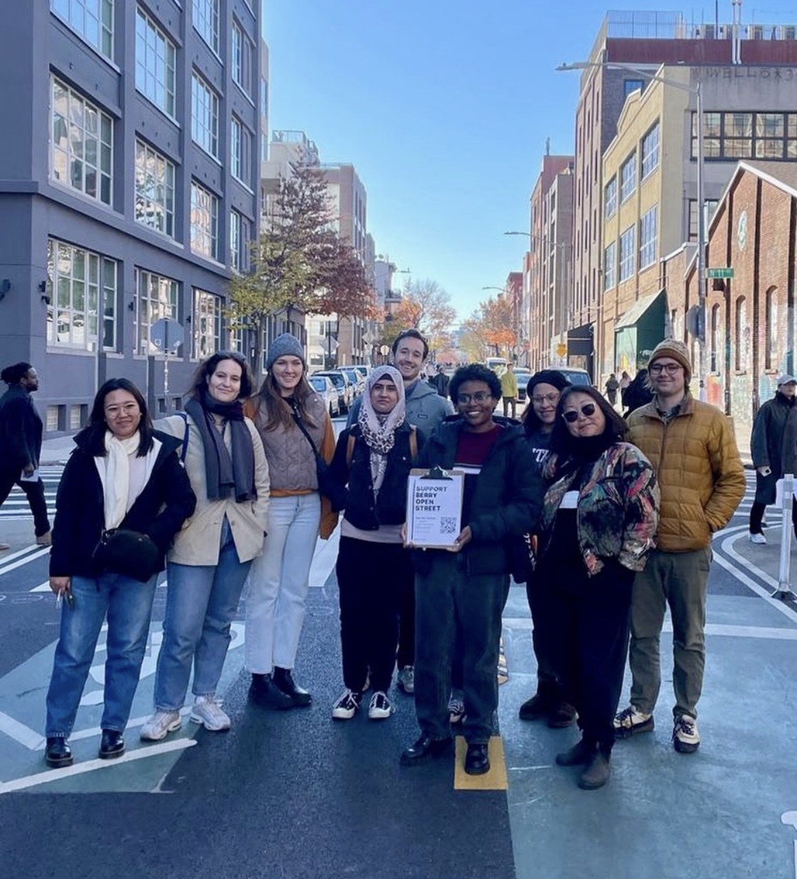 group of students, standing in a group and posing, view of berry street, south-facing, in williamburg brooklyn in background, students in foreground