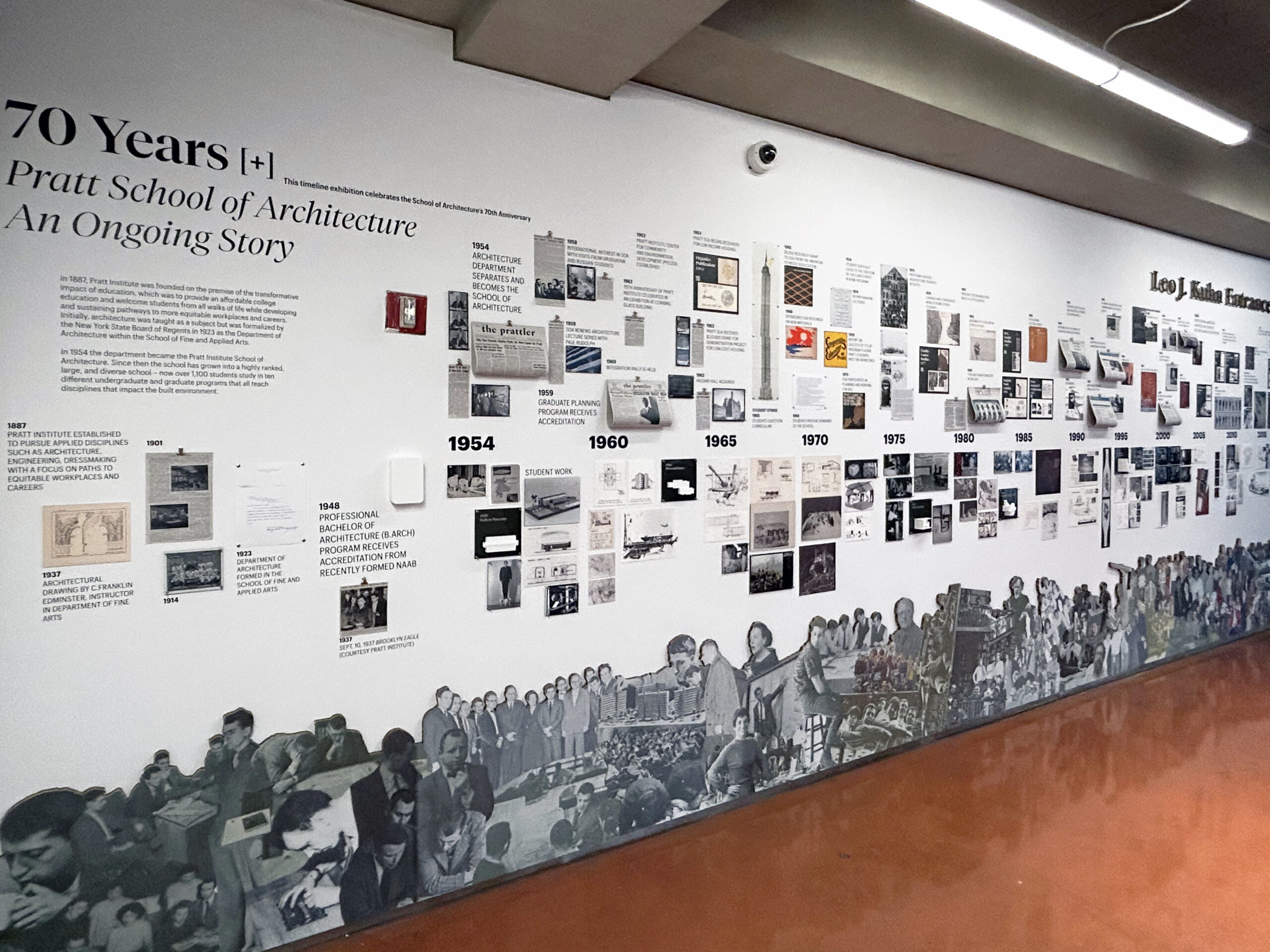 A timeline exhibition at the Pratt School of Architecture showcases its 70-year history with historical images, text, and a collage of people along the bottom.