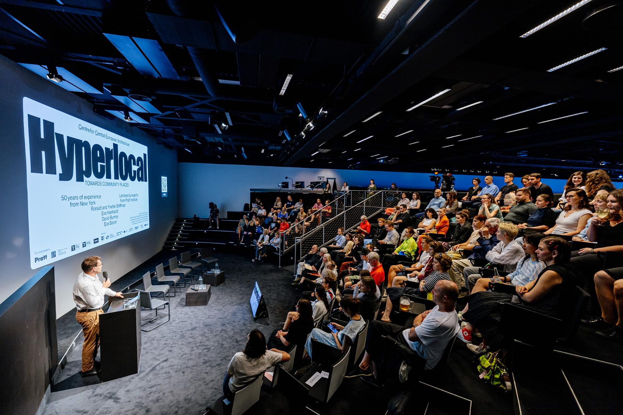 A lecture hall full of people listening to a presentation titled 