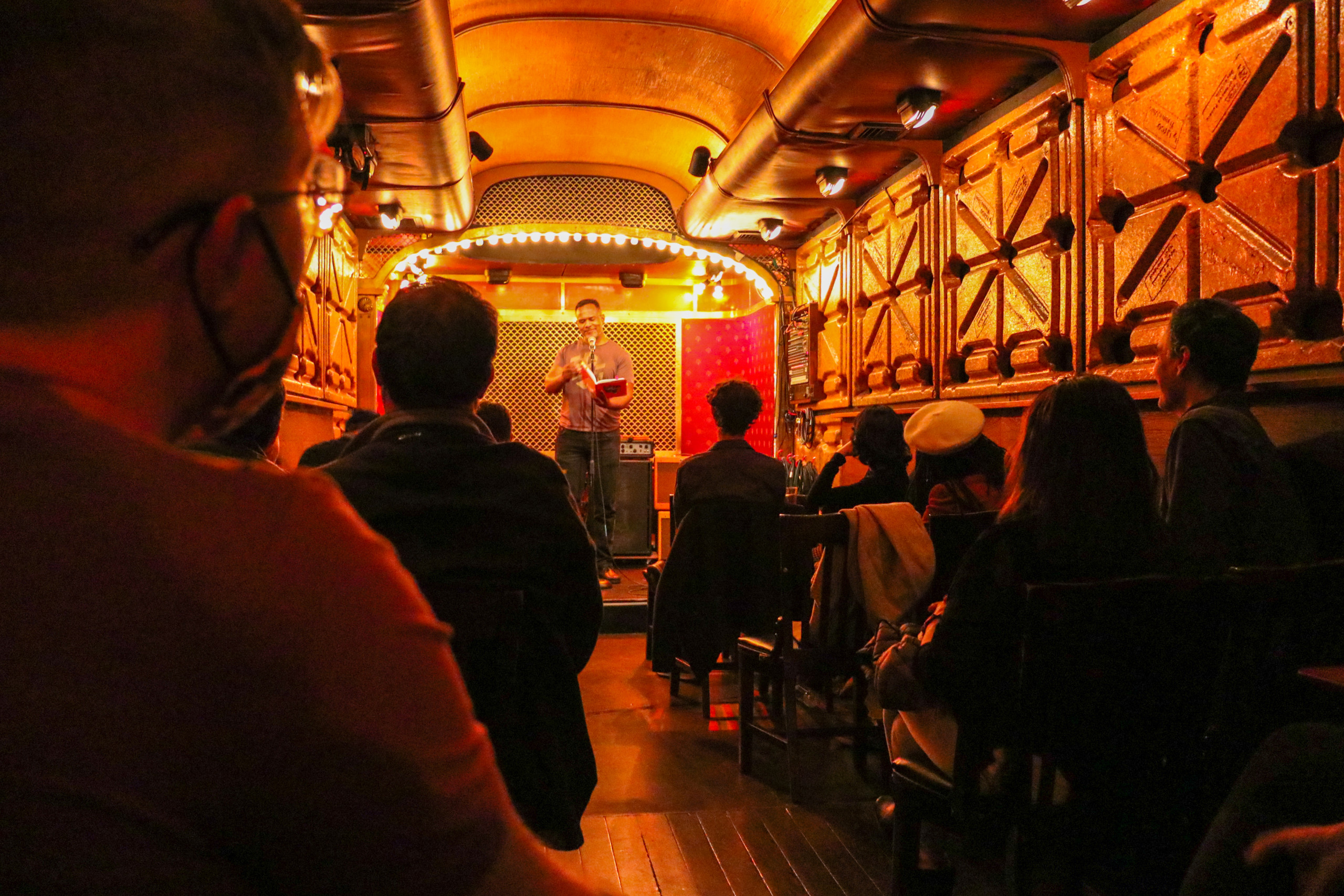 Author James Hannaham reads from a red book in a narrow venue lit in orange-red tones