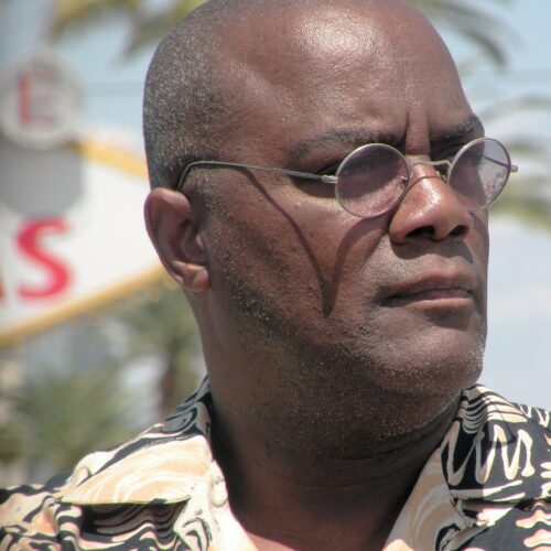 Close-up of a middle-aged man wearing sunglasses with a serious expression, set against an outdoor background.