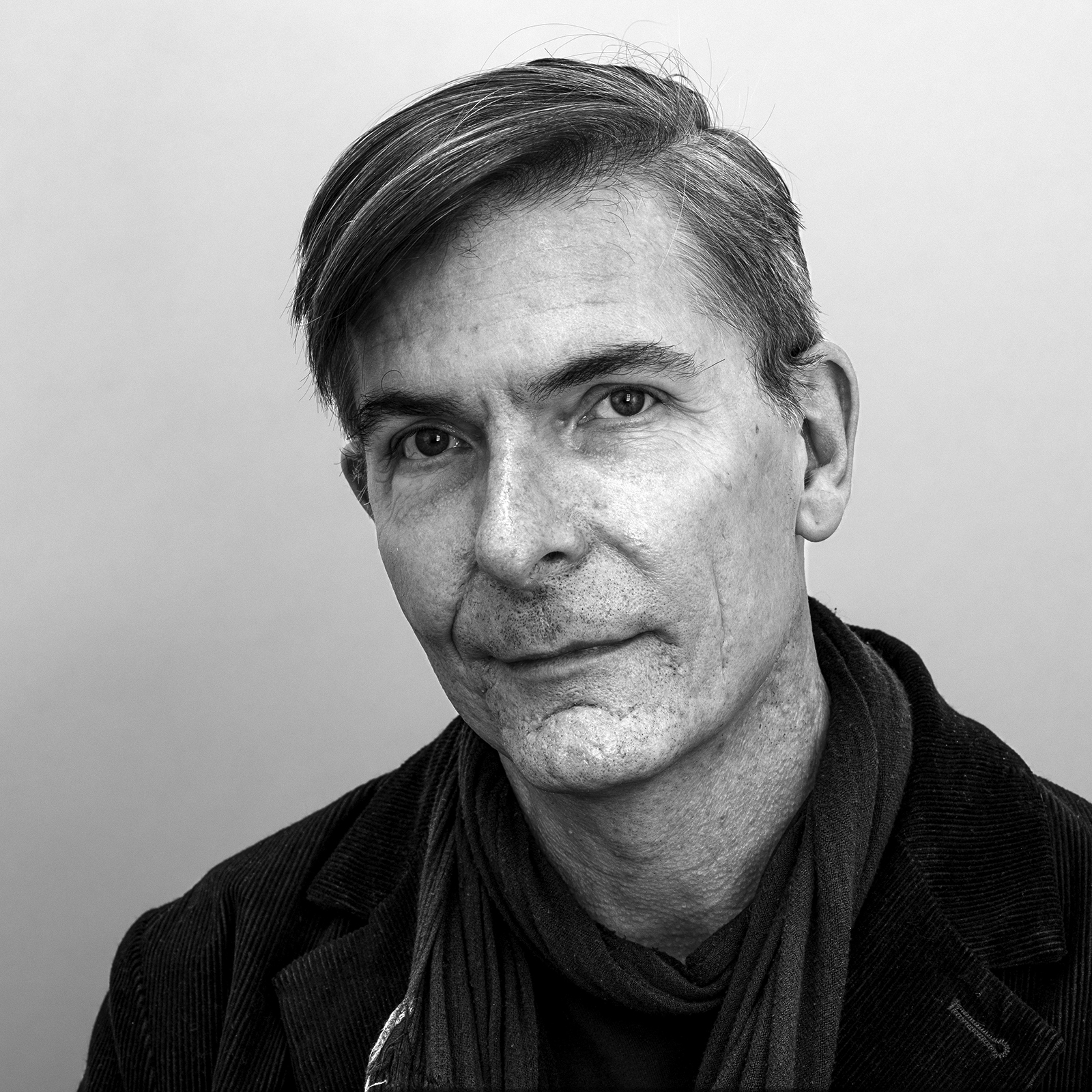 A black-and-white portrait of Alex Schweder, looking at the camera with a calm expression, wearing a scarf and a jacket.