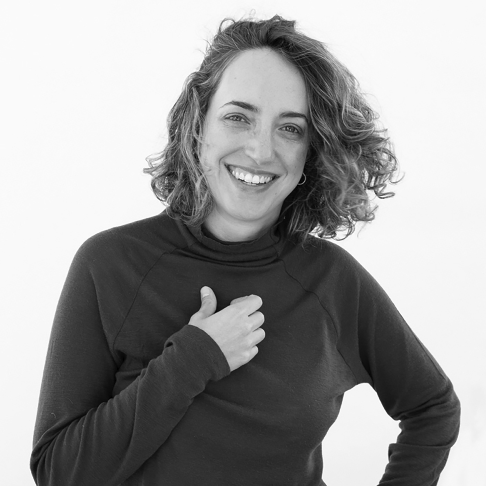 A black-and-white portrait of Esther Beke, smiling with one hand touching her chest, wearing a long-sleeved top.