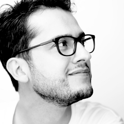 A grayscale image of Alvaro Uribe looking upwards with a slight smile. He is wearing glasses and a light shirt, with a plain white background.