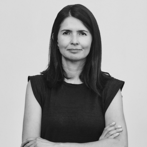 A grayscale portrait of Catalina Parra, a woman with straight hair wearing a sleeveless top, standing confidently with her arms crossed.