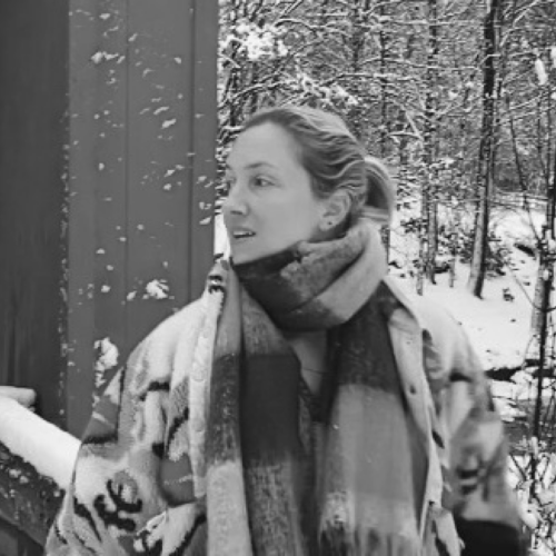 Emily Rothschild looks to her right while standing outdoors in a winter setting, bundled in a scarf and coat, snow-covered trees in the background.