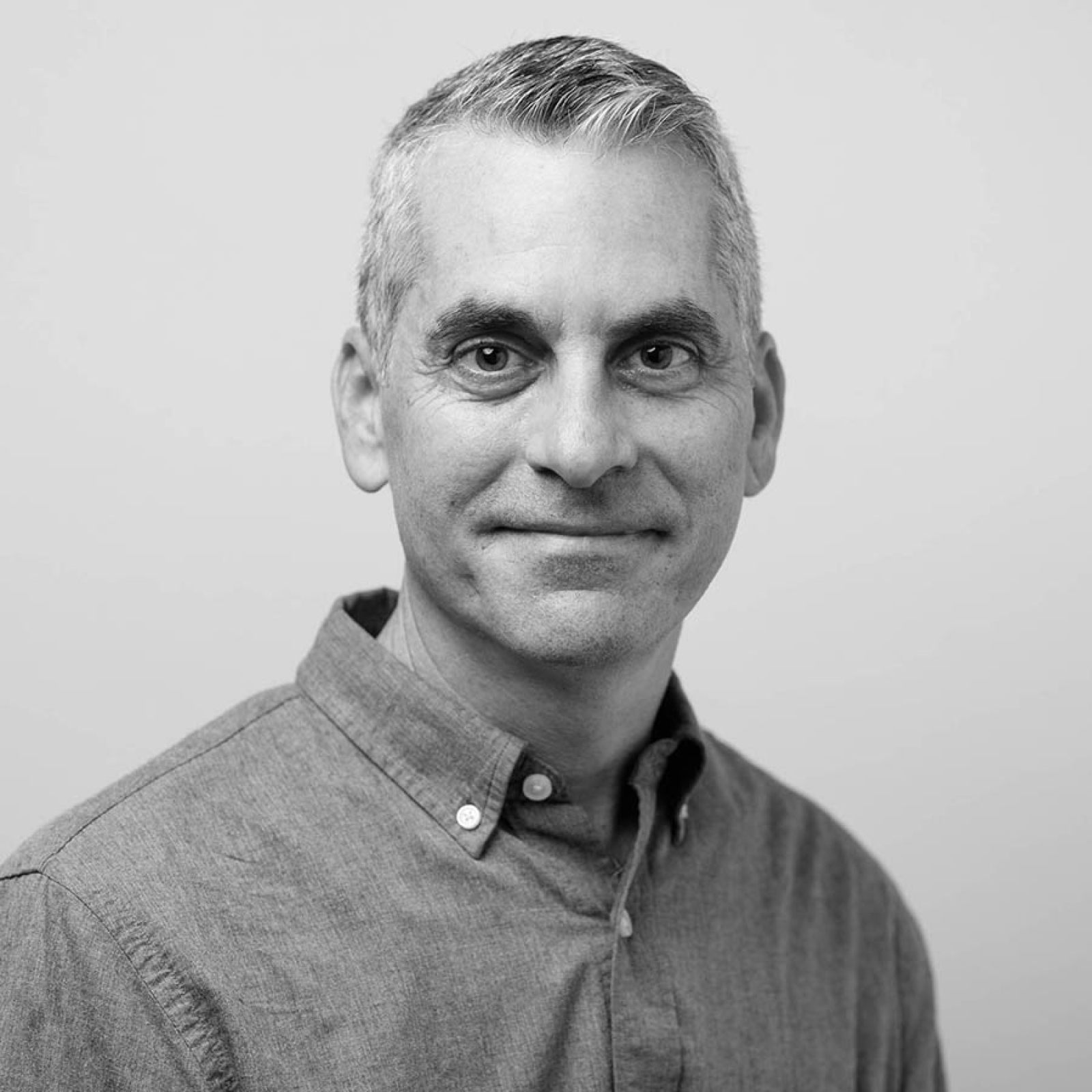 A grayscale portrait of a man with short, neatly combed gray hair, wearing a button-up shirt. He is smiling gently and looking directly at the camera.