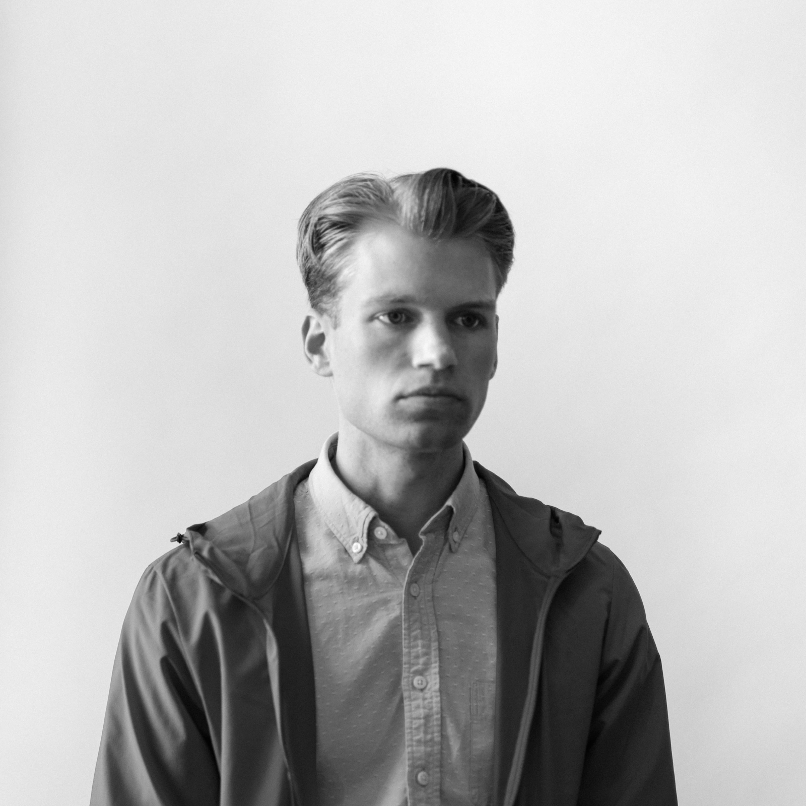 Josh Skirtish stands in front of a blank background, wearing a casual jacket and button-down shirt, looking serious.