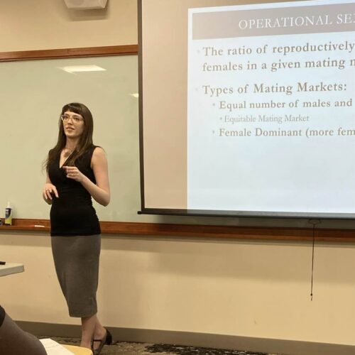 woman standing at blackboard projector, speaking