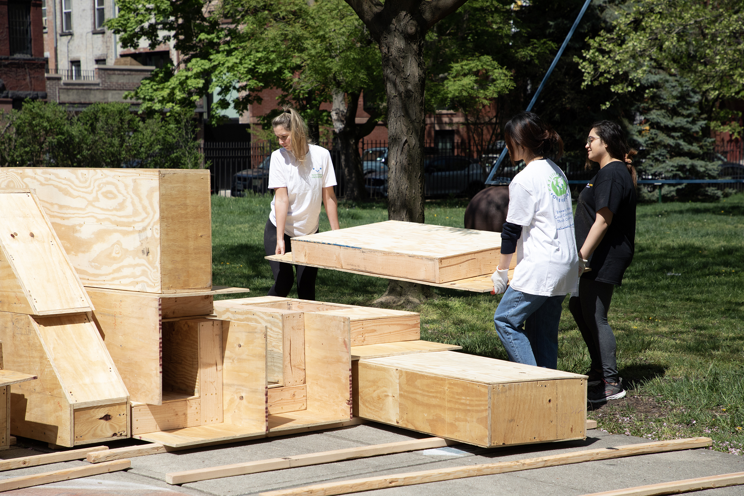 Students stack preassembled wood structural components during an architectural installation in a courtyard at Pratt Institute