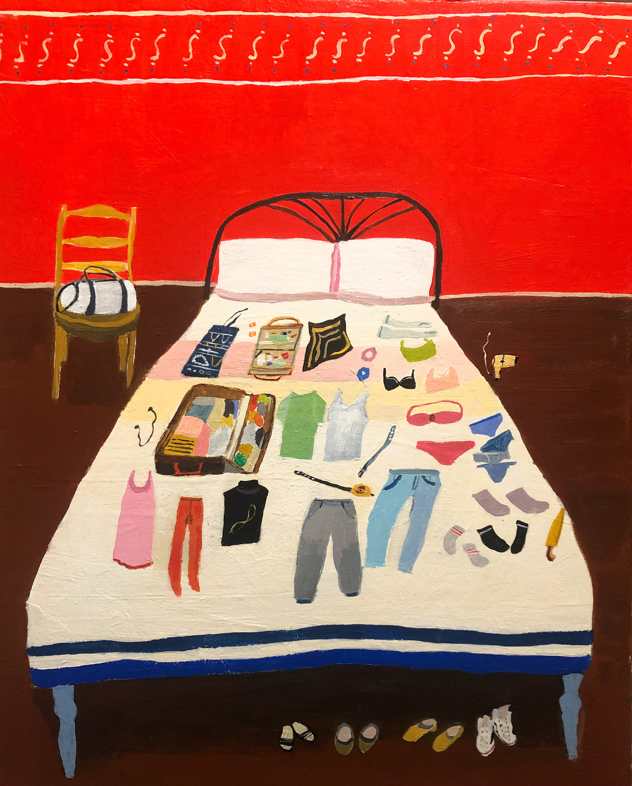 Clothing and accessories spread out neatly around a tidily packed suitcase on a white bed in front of a bright red wall