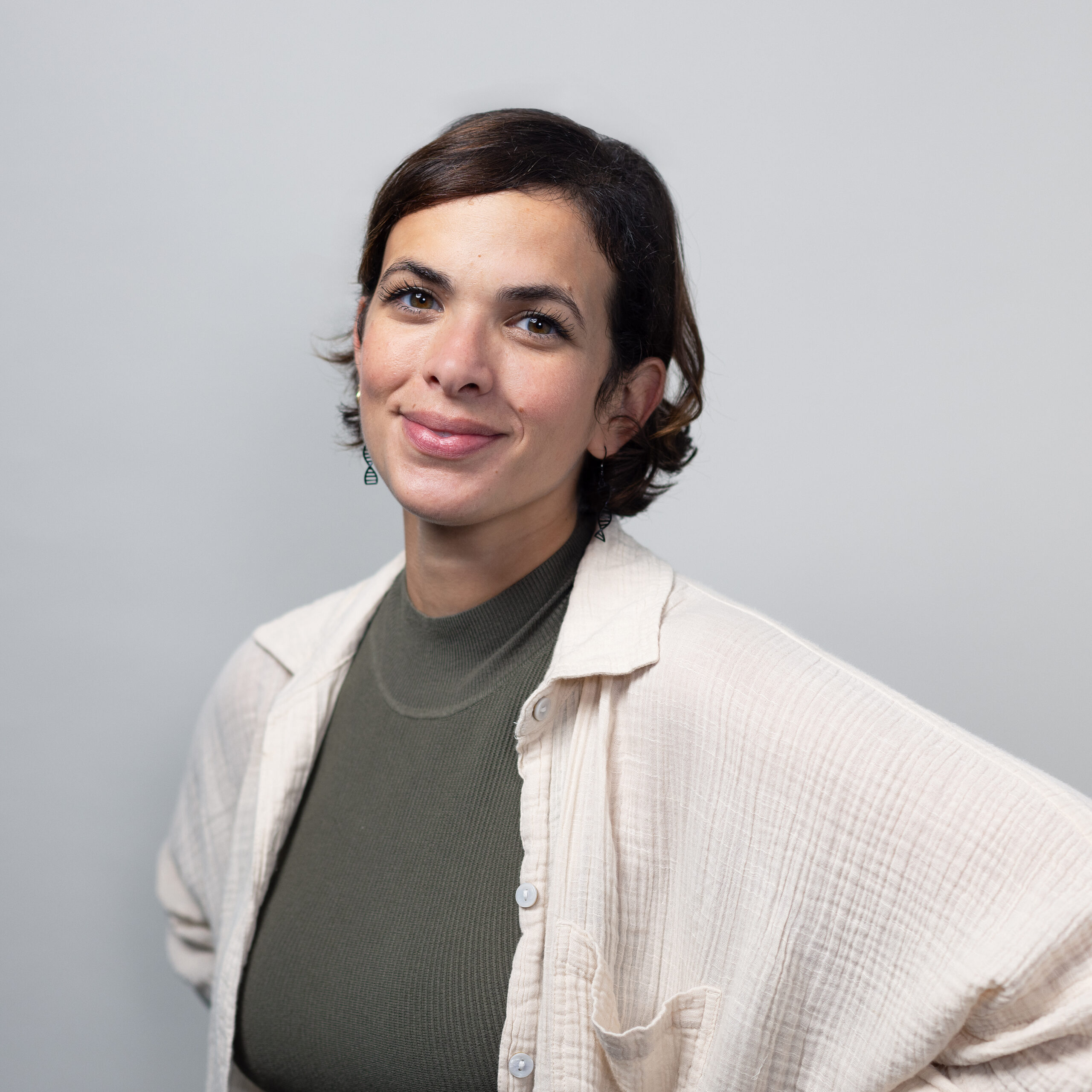 Portrait of a woman with short dark hair, wearing a beige cardigan over a green turtleneck, smiling at the camera with a soft expression.